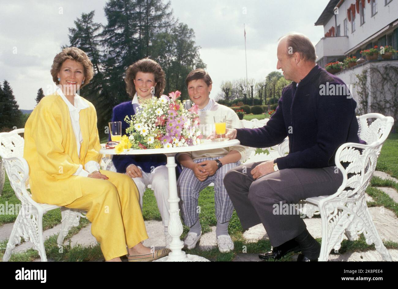 Skaugum 19870602 The Crown Prince family at Skaugum. Sitting at a garden table in the garden. From V: Crown Princess Sonja, Princess Märtha Louise, Prince Haakon Magnus and Crown Prince Harald. Sonja in yellow pants costume. Photo: Bjørn Sigurdsøn / NTB Stock Photo
