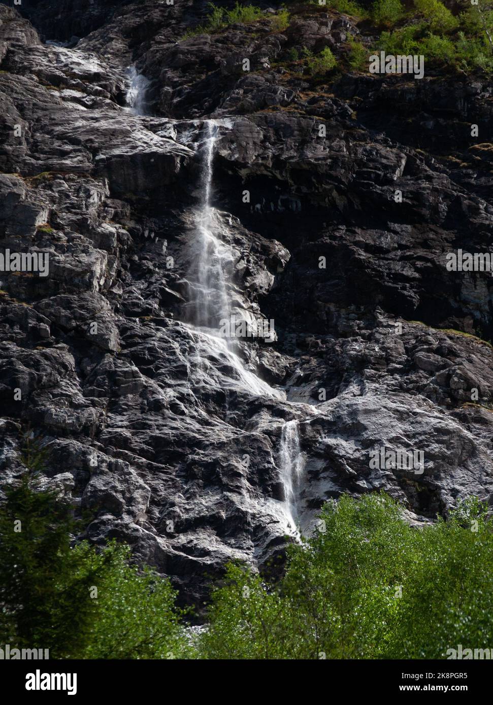 A vertical shot of a flowing waterfall on the side of a rocky mountain ...