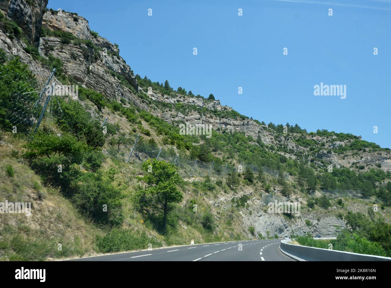 Mountain with safety fence to protect the road and cars from falling rocks. Heavy duty wire netting used to catch falling rocks from the cliffs in Stock Photo