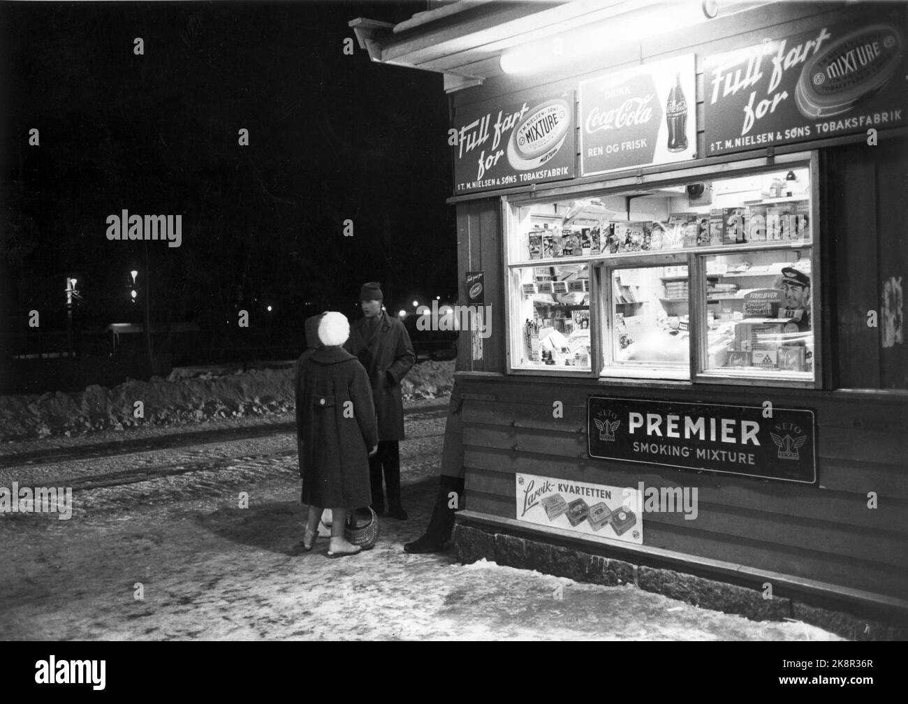Larvik 1960. What Norwegians do a Saturday night. Man and woman outside a kiosk. Night. Advertising. Divorced. Tobacco. Winter. Photo: Current / NTB Stock Photo
