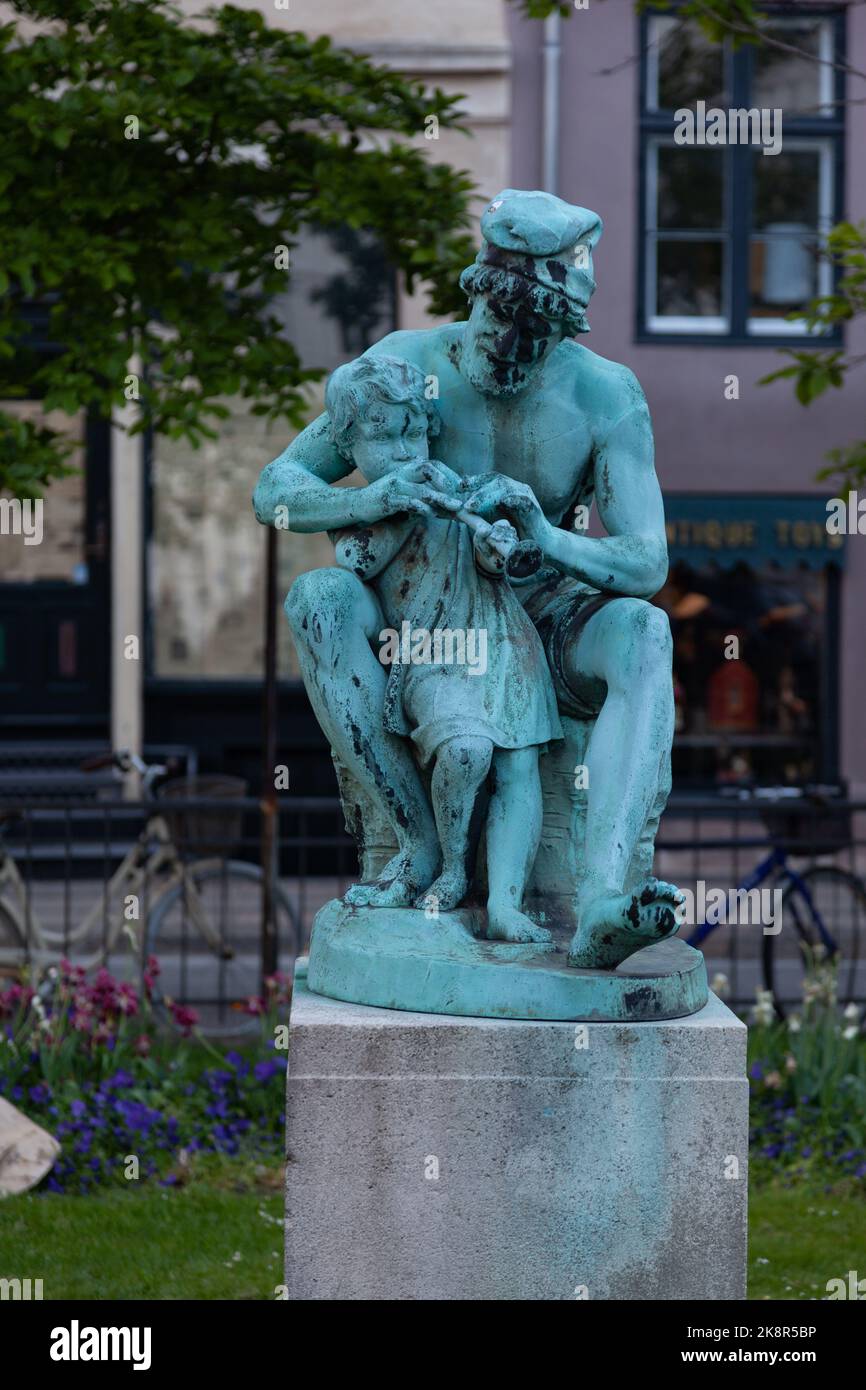 A vertical shot of a bronze statue of a fisherman teaching his son to play the flute in Copenhagen Stock Photo