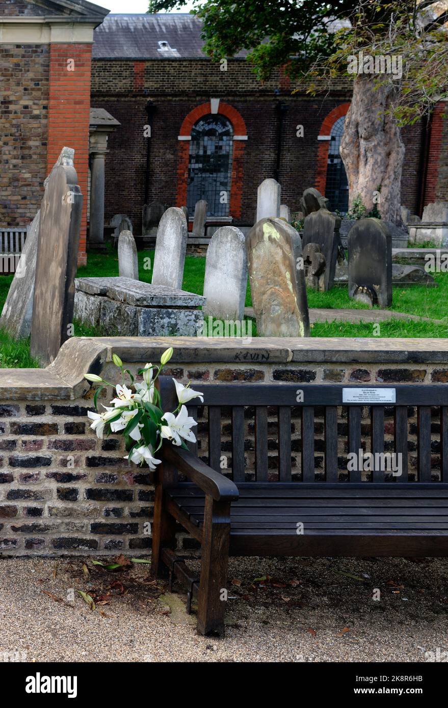 Flowers on a bench of remembrance whilst the gravestones behind have none, Kew Green, London, England Stock Photo