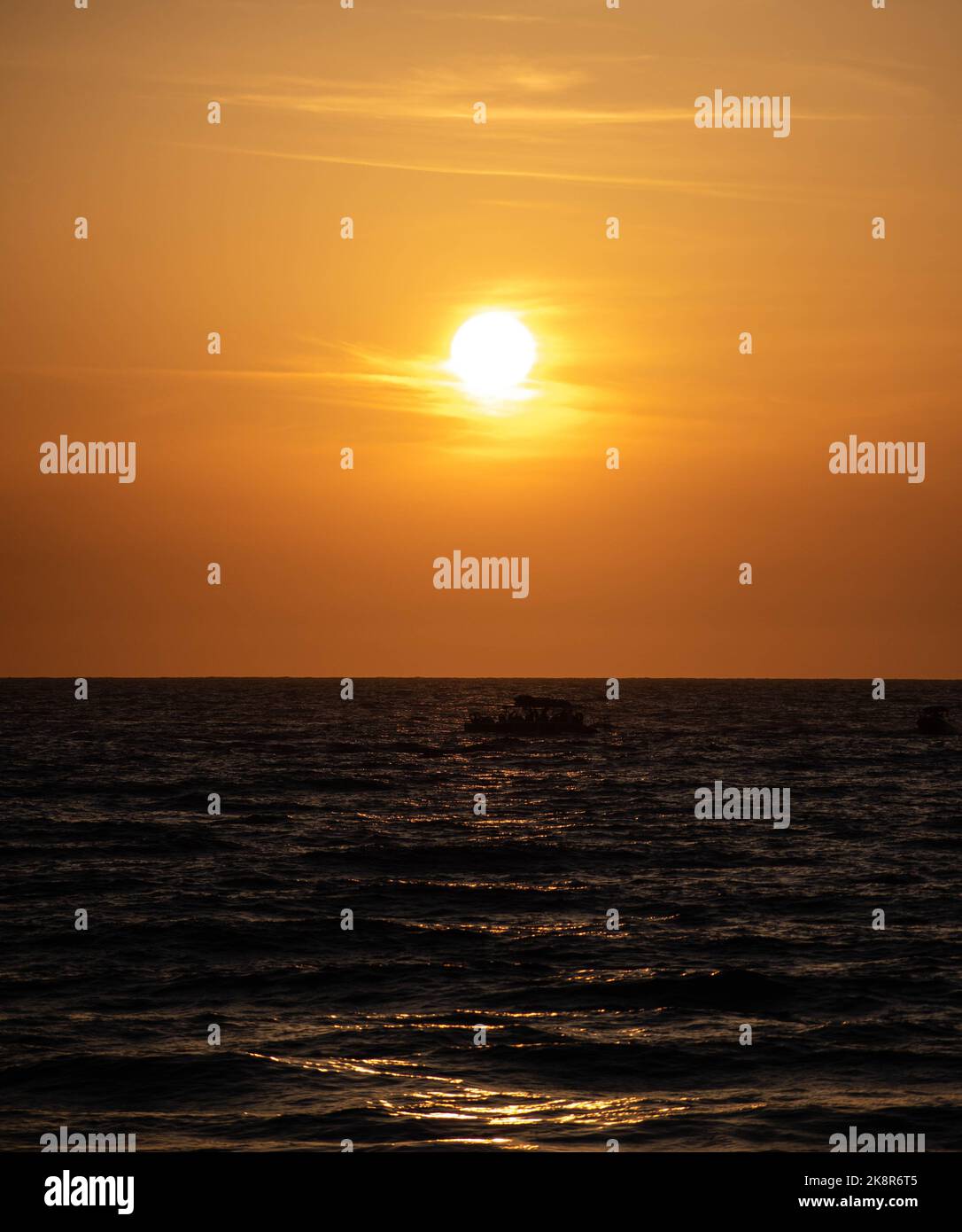 A dramatic golden sunset over the sea with a silhouette of a small ...