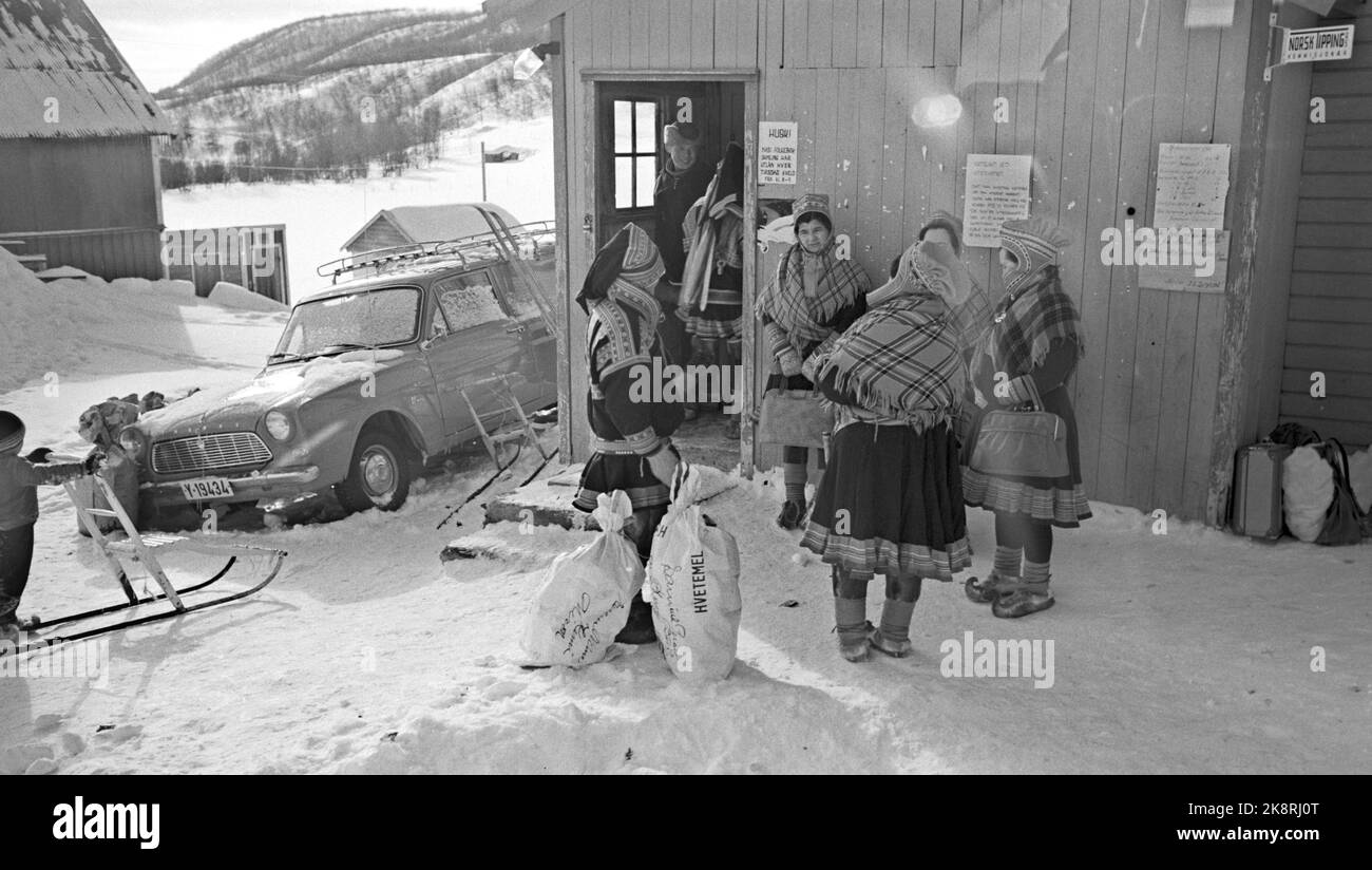 Finnmark 19650410 Caught by Finnmarksvidda -One of this year's travel news is winter trips to Finnmarksvidda. Also without the midnight sun, the region has a lot to offer the tourists: Meeting with Sami and reindeer, magnificent skiing and beautiful scenery. It is Bennett Reiseburå that arranges the trips north. The tickets at a price of NOK. 1295,- for 9 days trip, all incuded, was torn away. Here: Women and men outside wooden houses. Car parked. Photo: Aage Storløkken / Current / NTB Stock Photo