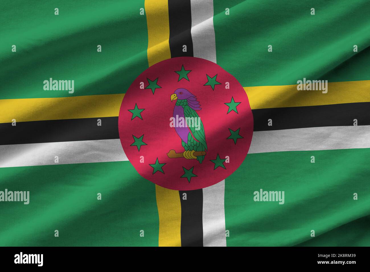 Dominica flag with big folds waving close up under the studio light indoors. The official symbols and colors in fabric banner Stock Photo