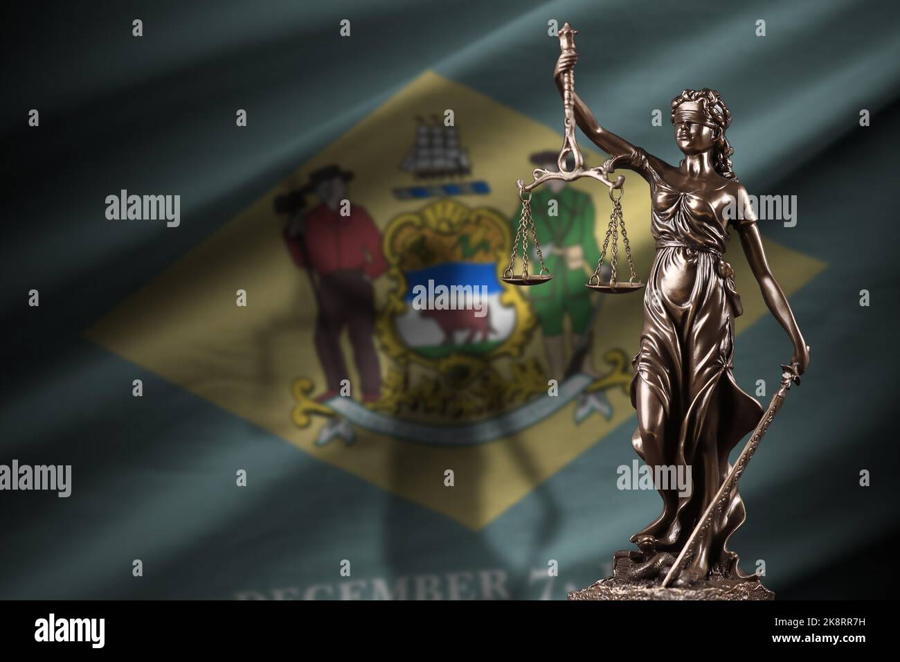 Delaware US state flag with statue of lady justice and judicial scales in dark room. Concept of judgement and punishment, background for jury topics Stock Photo