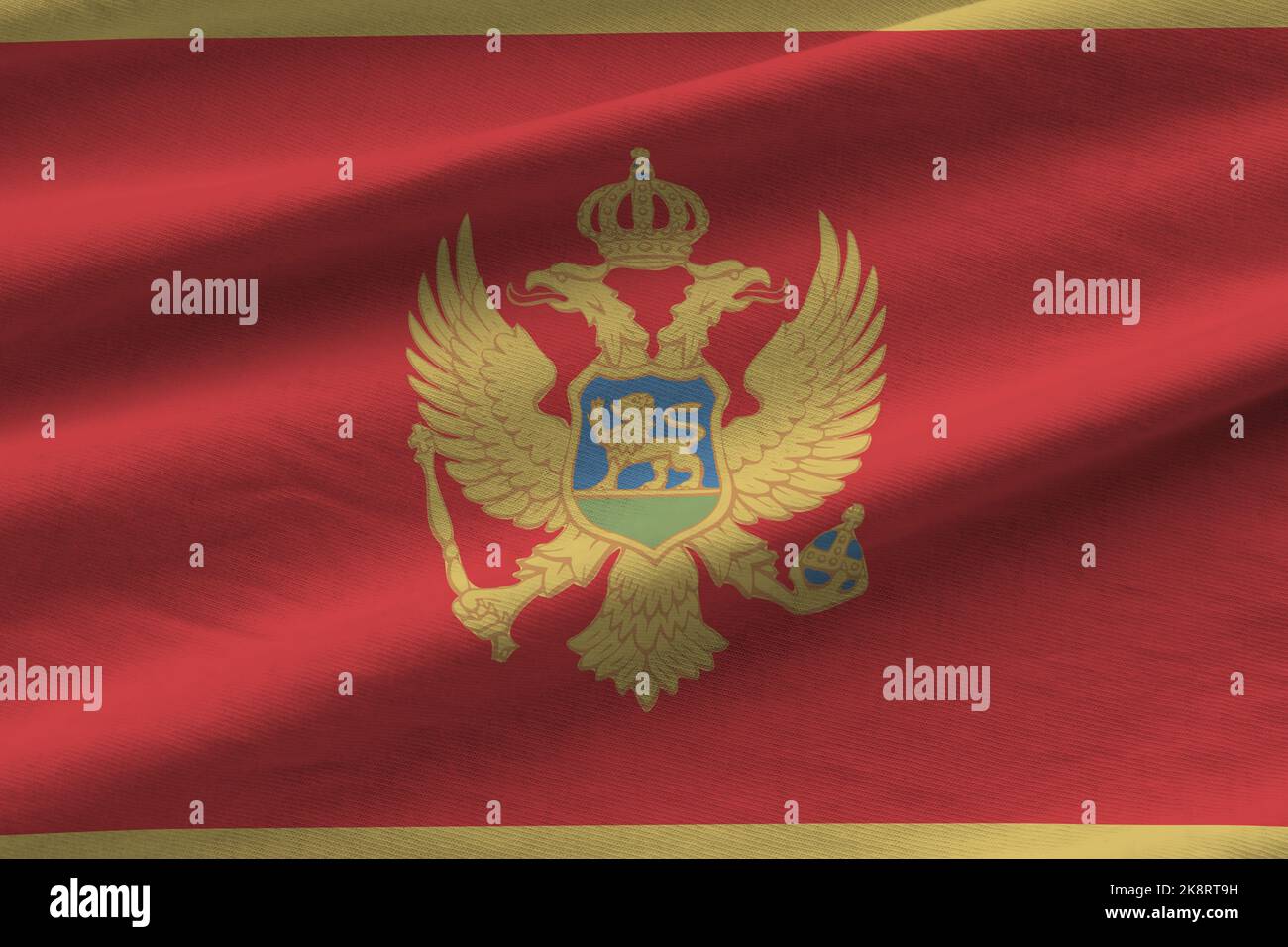 Montenegro flag with big folds waving close up under the studio light indoors. The official symbols and colors in fabric banner Stock Photo