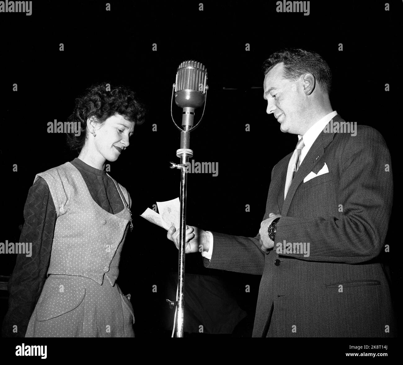 Oslo 1955 NRK Radio has a great success with the questionnaire 'The question' led by the big jar Rolf Kirkvaag. The concept is simple and the prizes are modest but the mood in the studio is at the boiling point! Here Kirkvaag in action with one of the participants. 'Do they move on?' Kirkvaag asks and fans with Tierne. Large old -fashioned microphone in the middle of the picture. Photo: Storløkken / Current / NTB Stock Photo