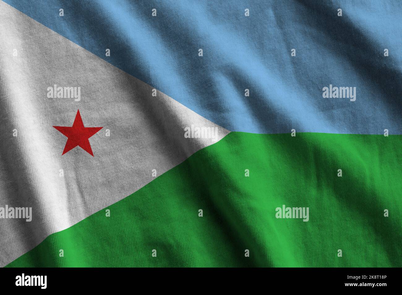 Djibouti flag with big folds waving close up under the studio light indoors. The official symbols and colors in fabric banner Stock Photo