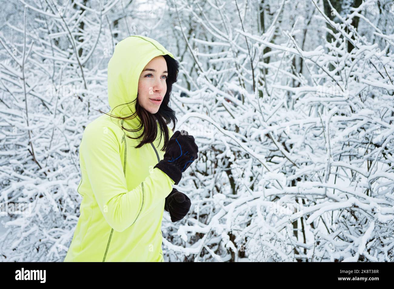 Cold Weather Running. Happy woman running in winter snowy park, forest. Running athlete woman sprinting during winter training outside in cold snow Stock Photo