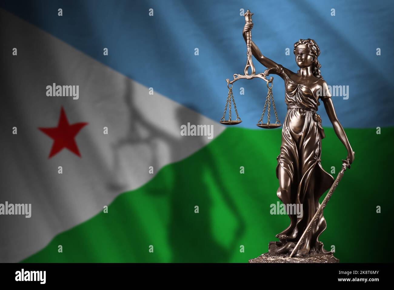 Djibouti flag with statue of lady justice and judicial scales in dark room. Concept of judgement and punishment, background for jury topics Stock Photo