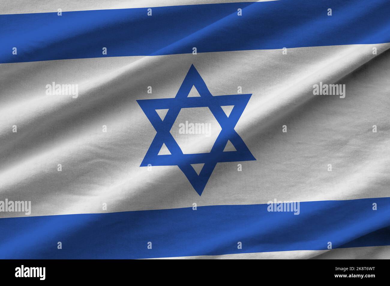 Israel flag with big folds waving close up under the studio light indoors. The official symbols and colors in fabric banner Stock Photo