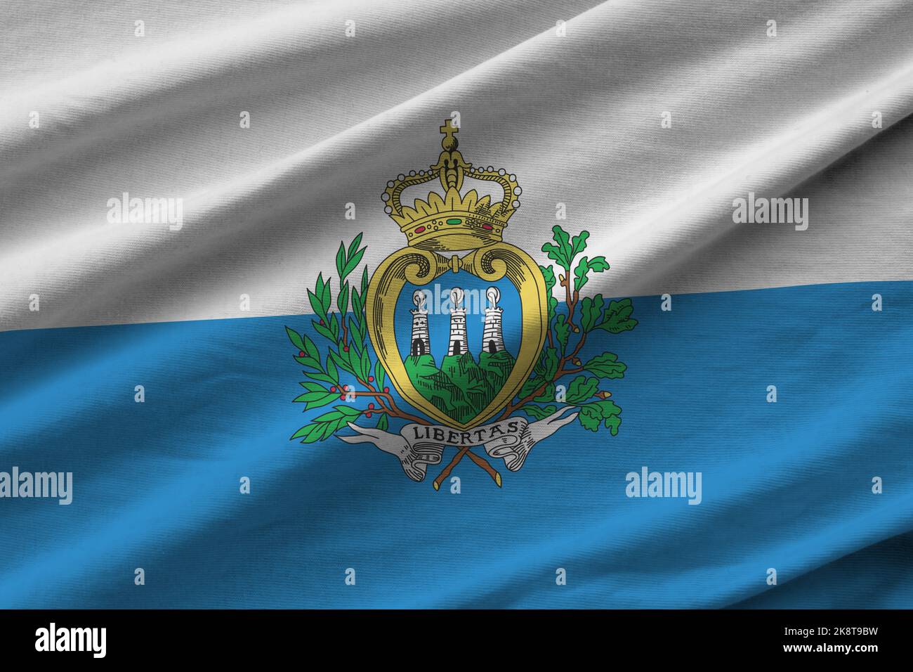 San Marino flag with big folds waving close up under the studio light indoors. The official symbols and colors in fabric banner Stock Photo