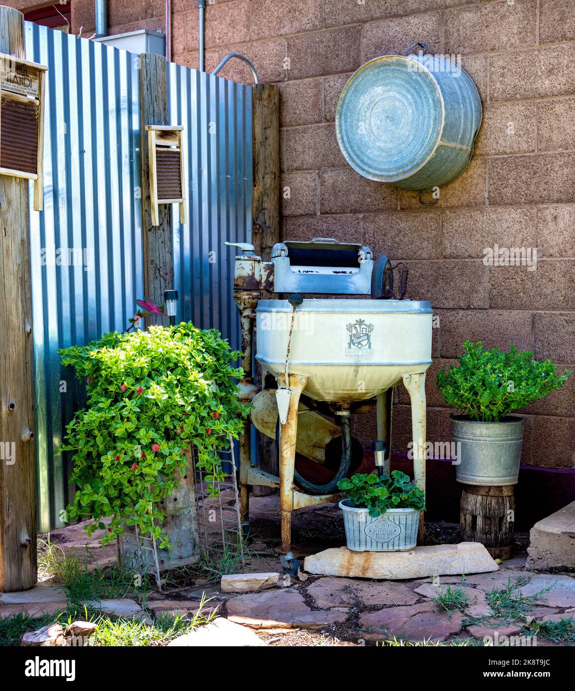 A vertical shot of vintage washing machine and green plants against stone wall in the backyard Stock Photo