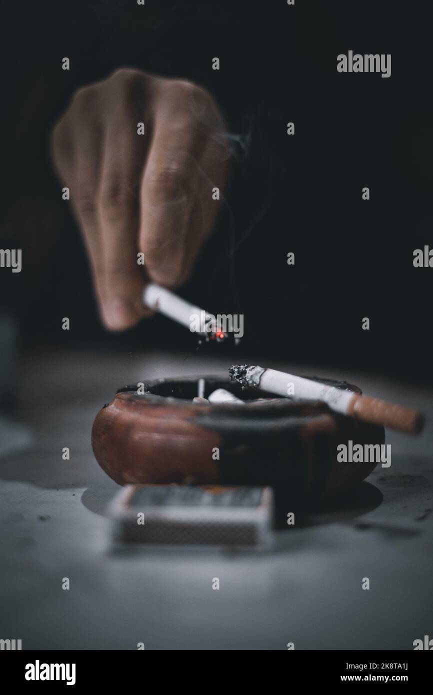 A vertical shot of a hand in a dark background flicking cigarette ash