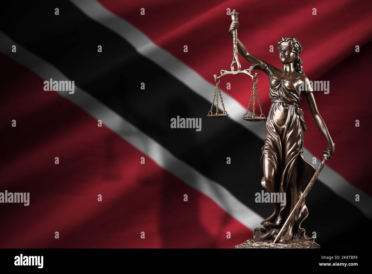 Trinidad and Tobago flag with statue of lady justice and judicial scales in dark room. Concept of judgement and punishment, background for jury topics Stock Photo