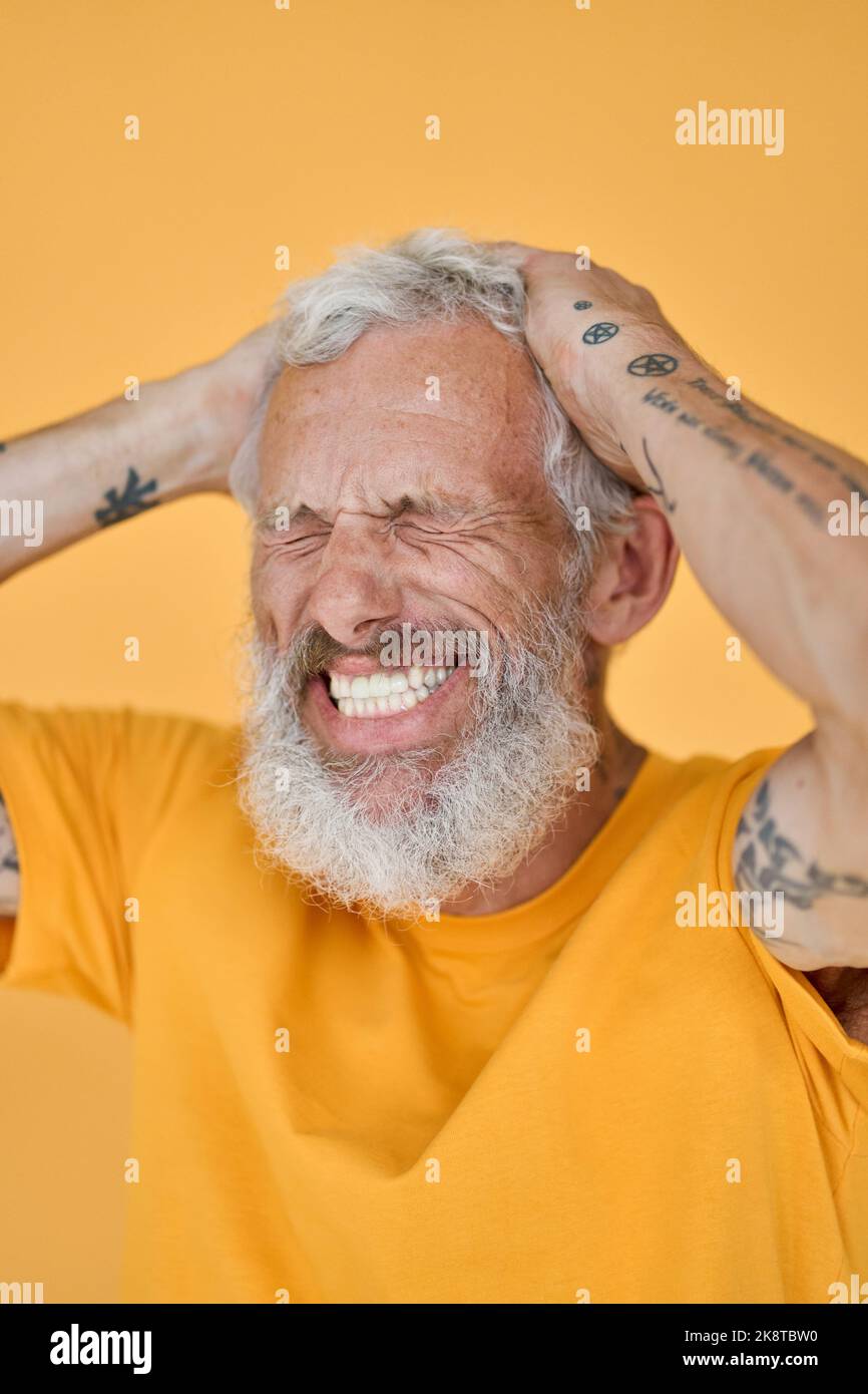 Happy funny older bearded tattooed man laughing isolated on yellow. Stock Photo