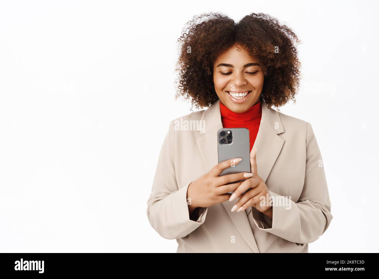 Image of smiling african american saleswoman records video on mobile phone, takes photo, shoots on smartphone, stands over white background Stock Photo