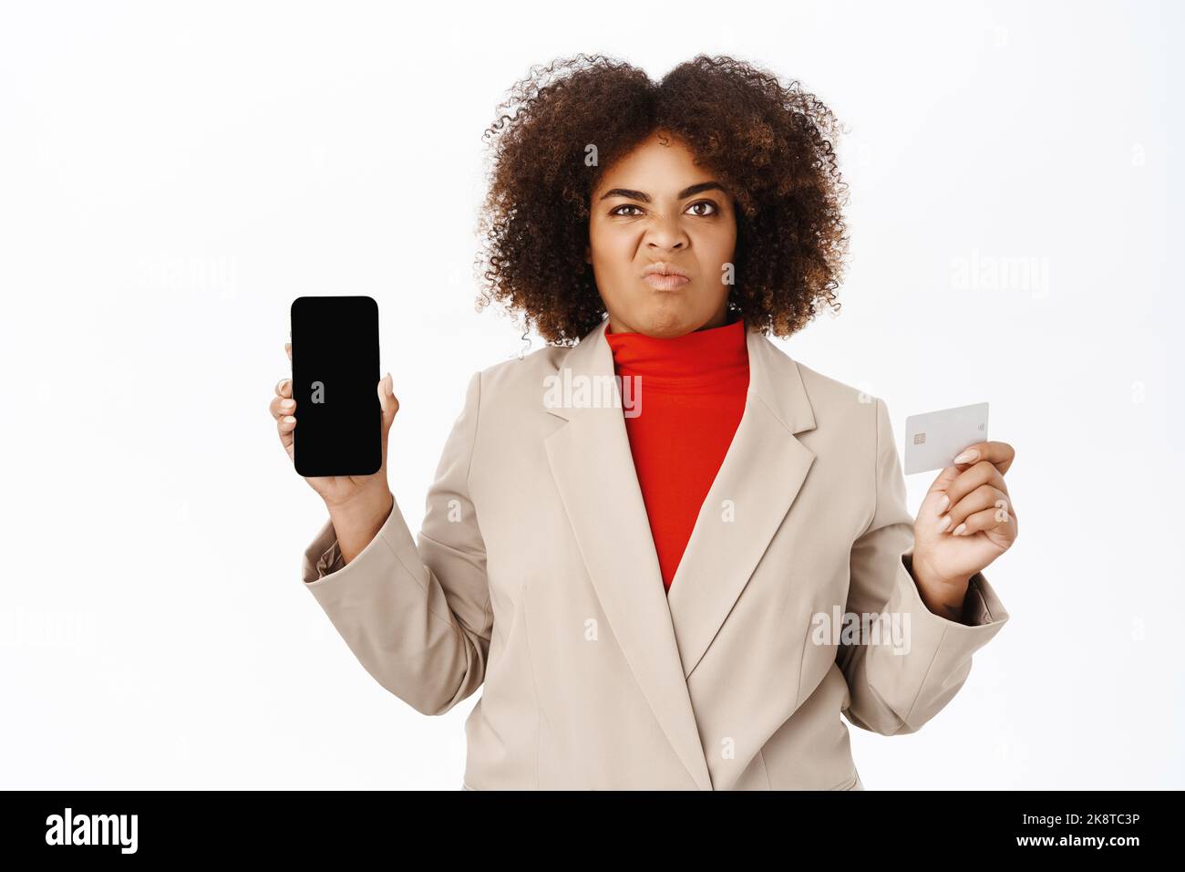 Disappointed african american businesswoman shows telephone screen, mobile interface and credit card, express dislike, stands over white background Stock Photo