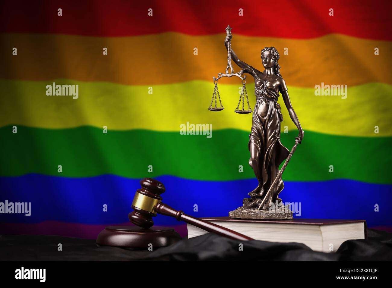 LGBT community flag with statue of lady justice, constitution and judge hammer on black drapery. Concept of judgement and punishment Stock Photo