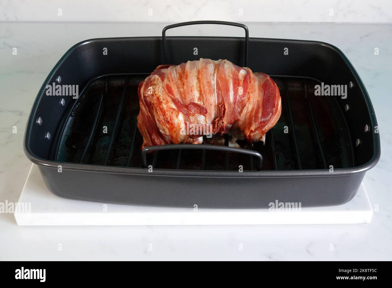 A delicious roast turkey crown wrapped with bacon in a black baking tray Stock Photo