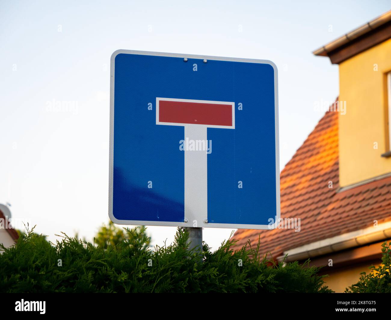 German dead end road sign. A red horizontal beam and a white beam is on a blue ground. The traffic sign is in a square shape. The street is ending. Stock Photo