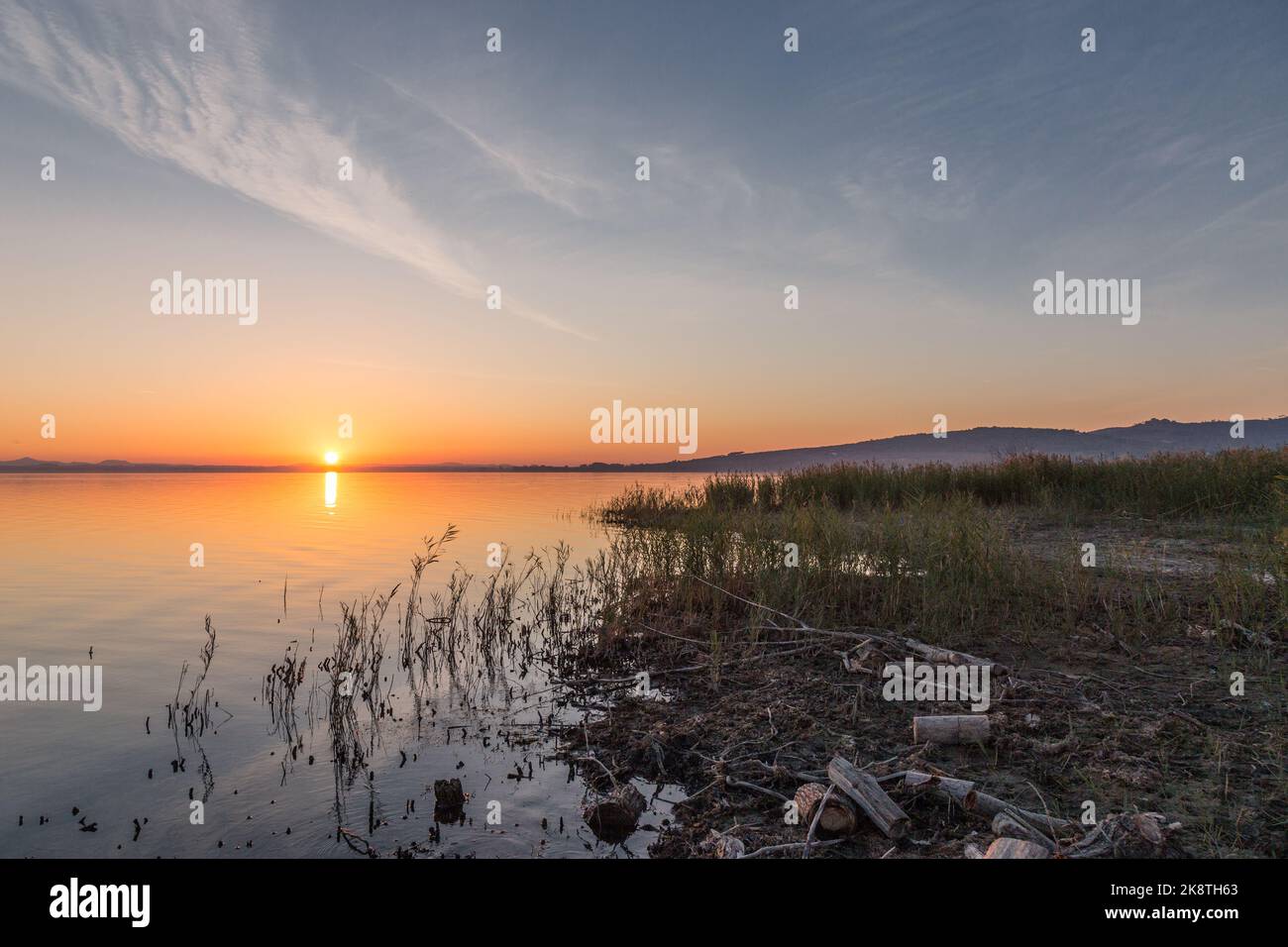 Lake shore at sunset with sun reflecting on water Stock Photo - Alamy