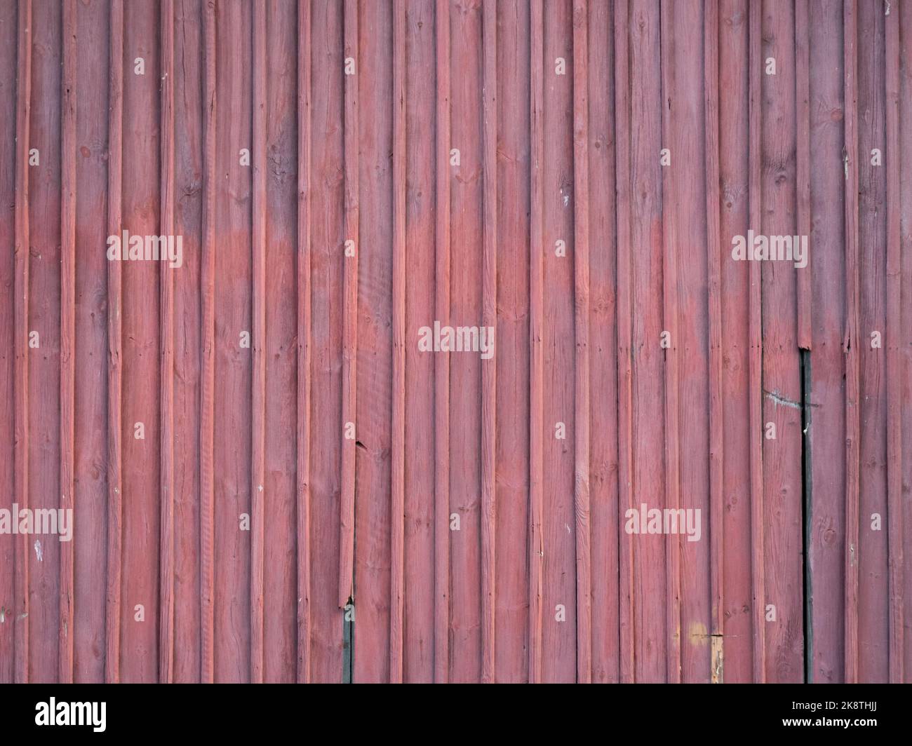 Red wooden planks background. Partially broken and weathered boards. Texture of a building exterior of an old house. A vertical design pattern. Stock Photo