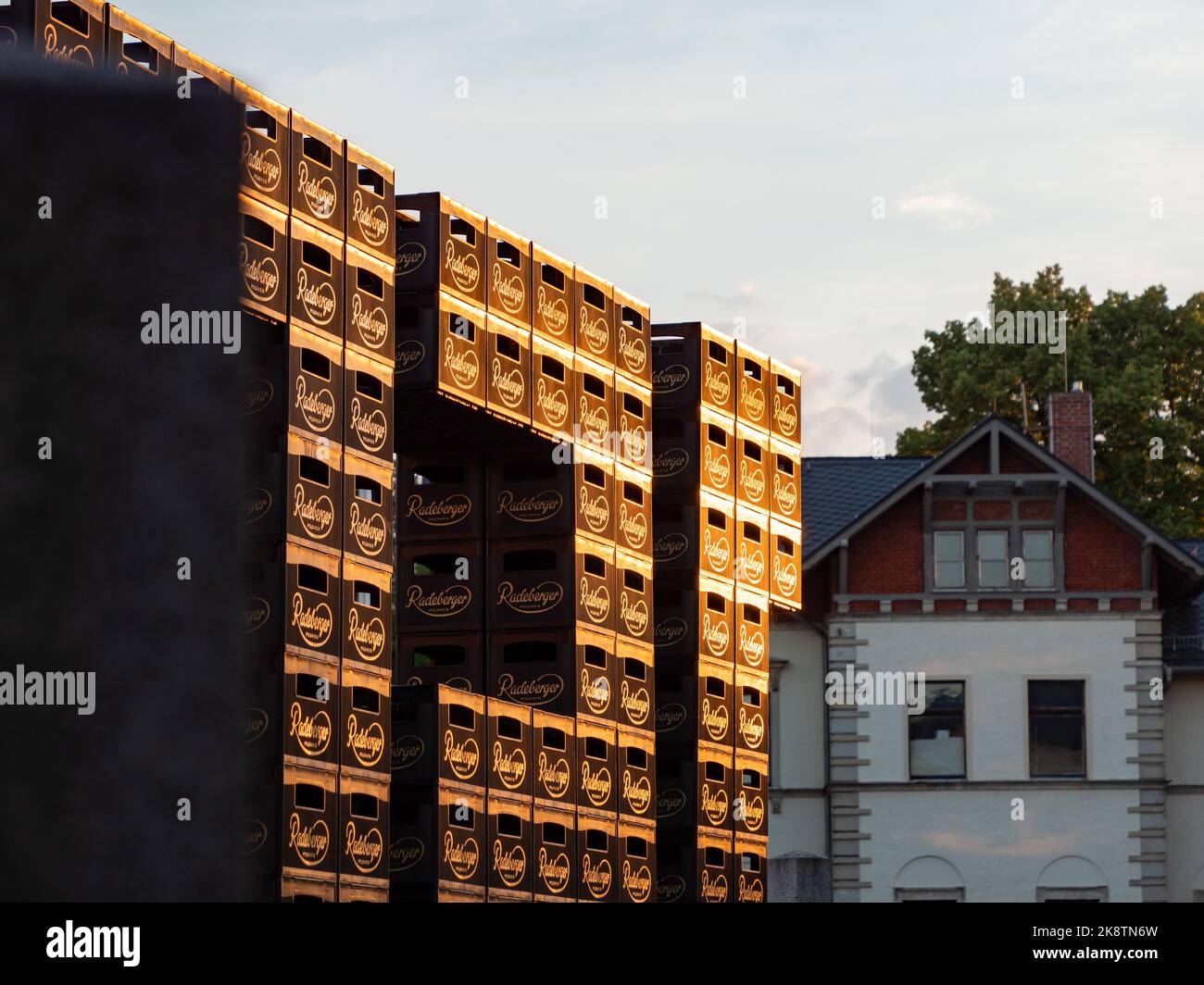 Radeberger pilsner beer crates stacked on top of each other. The golden logos are illuminated by evening sunlight. The crates are at the brewery. Stock Photo