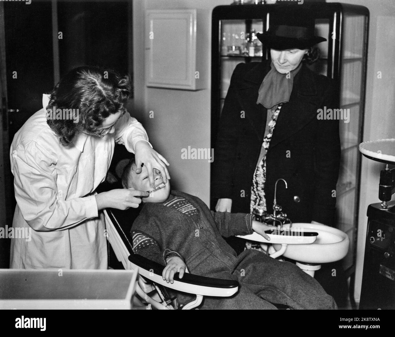 Oslo 1941: Oslo Municipal folk kan care in Møllergata 24. Little boy in the dental chair. Female dentist shows how to polish the teeth. The boy's mother comes along from the side. Photo: NTB Stock Photo