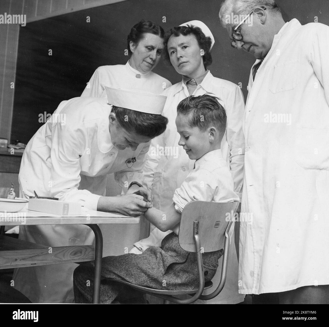 Nes at Romerike, 19561016: The first vaccination against poliomylitis started at Framtun school at Nes at Romerike. Health sister Ruth Hauge vaccinates the first student Ola Eide. District physician Øverland and the nurses Borghild Henden and Signe Berg follow. Photo: Aage Storløkken / Current / NTB Stock Photo