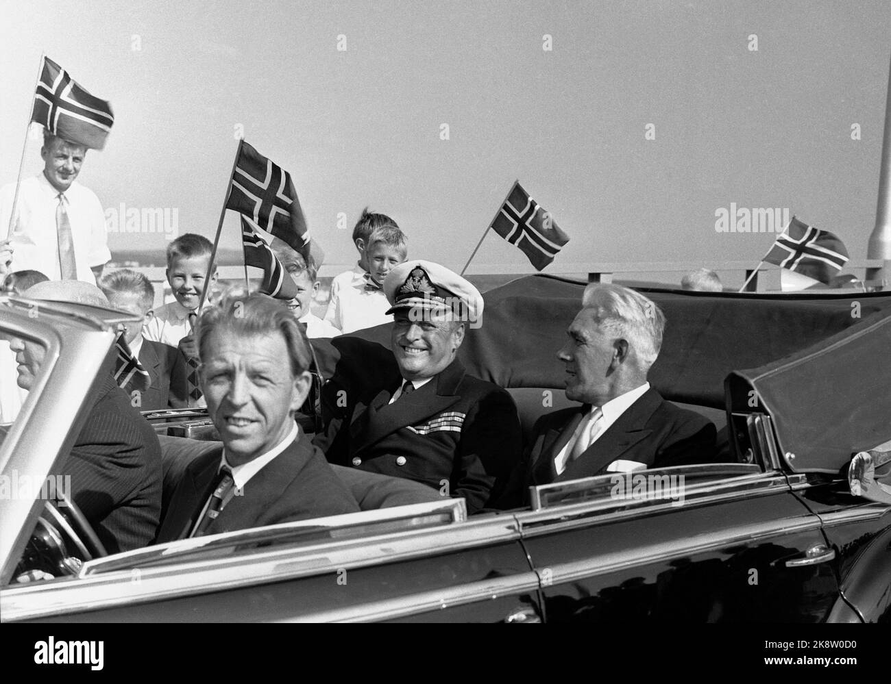 Fredrikstad 19570718 Crown Prince Olav arrives for the opening of the Fredrikstad Bridge,- bridge over Glomma between Østre and Vestre Fredrikstad. A smiling crown prince in uniform in a car, flag in the background. Photo: Jan Nordby / NTB / NTB Stock Photo