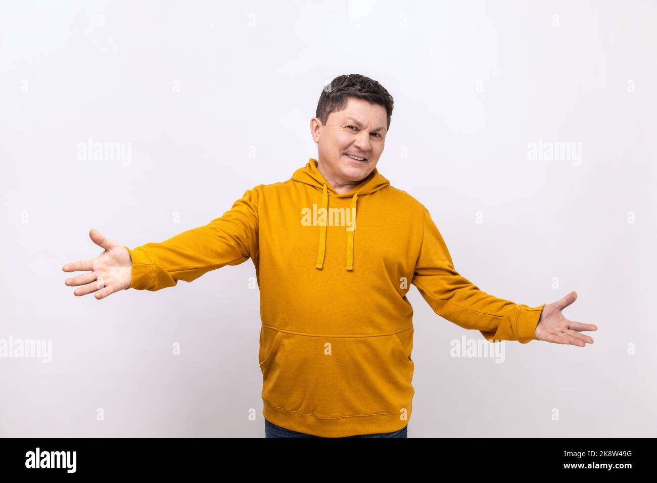 Welcome, wide open hug. Middle aged man stretching hands to camera and smiling broadly, going to embrace, share love, wearing urban style hoodie. Indoor studio shot isolated on white background. Stock Photo