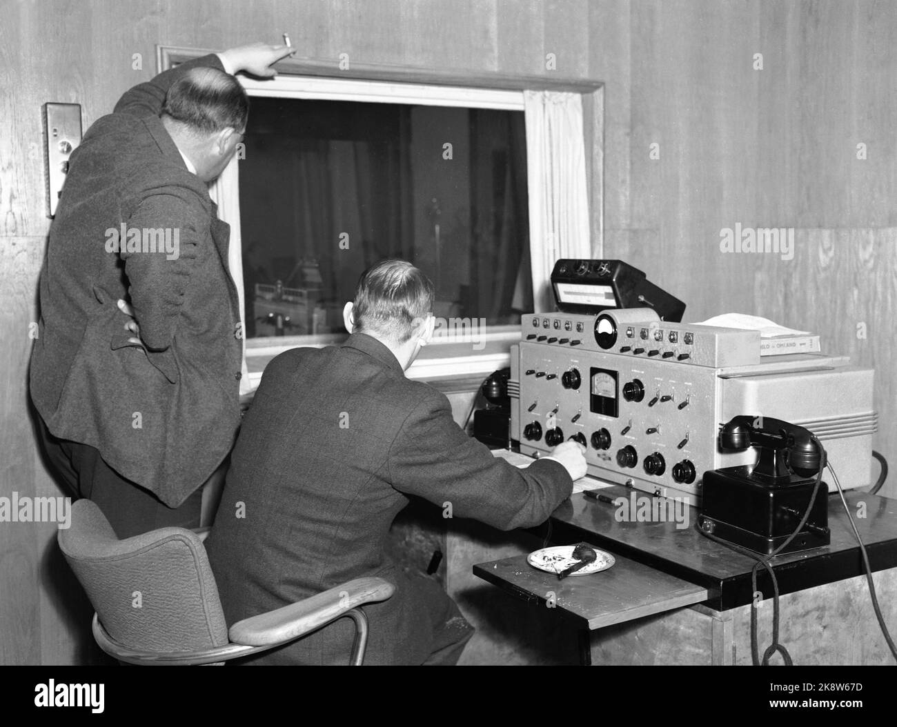 Oslo 19461026: Norwegian National Broadcasting (NRK) - Technical equipment from the post -war NRK. At that time it was only radio. Here technical equipment in the control room. An old telephone device on the table. - This was before the smoking law - one man smokes a cigarette, the other has a pipe lying ready. Photo: H.A.A. Stock Photo