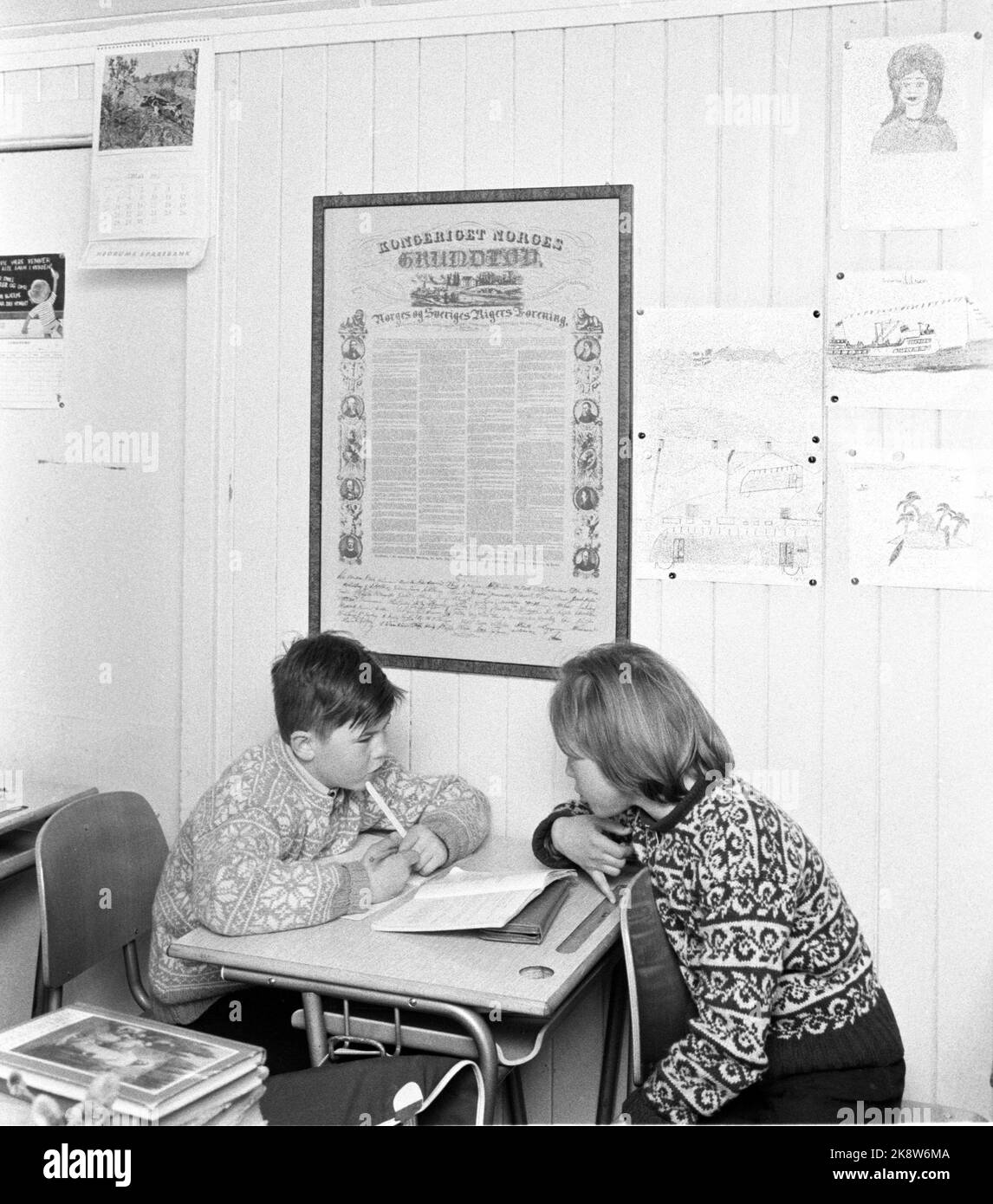 Komagfjord, Finnmark, 1962 Discipline problems are not found at Komagfjord school, but otherwise they lack everything. They have never had a qualified teacher, the air in the classroom is lousy, the textbooks are obsolete. There is no focus on school, because the children could have gone to the new Korsfjord school half a mile away - if it had been the way there ... and while politicians are arguing, life goes on the small school. Here are two of the children working in the classroom. The Constitution hangs on the wall, along with its own children's drawings. Photo: Aaserud / Current / NTB Stock Photo