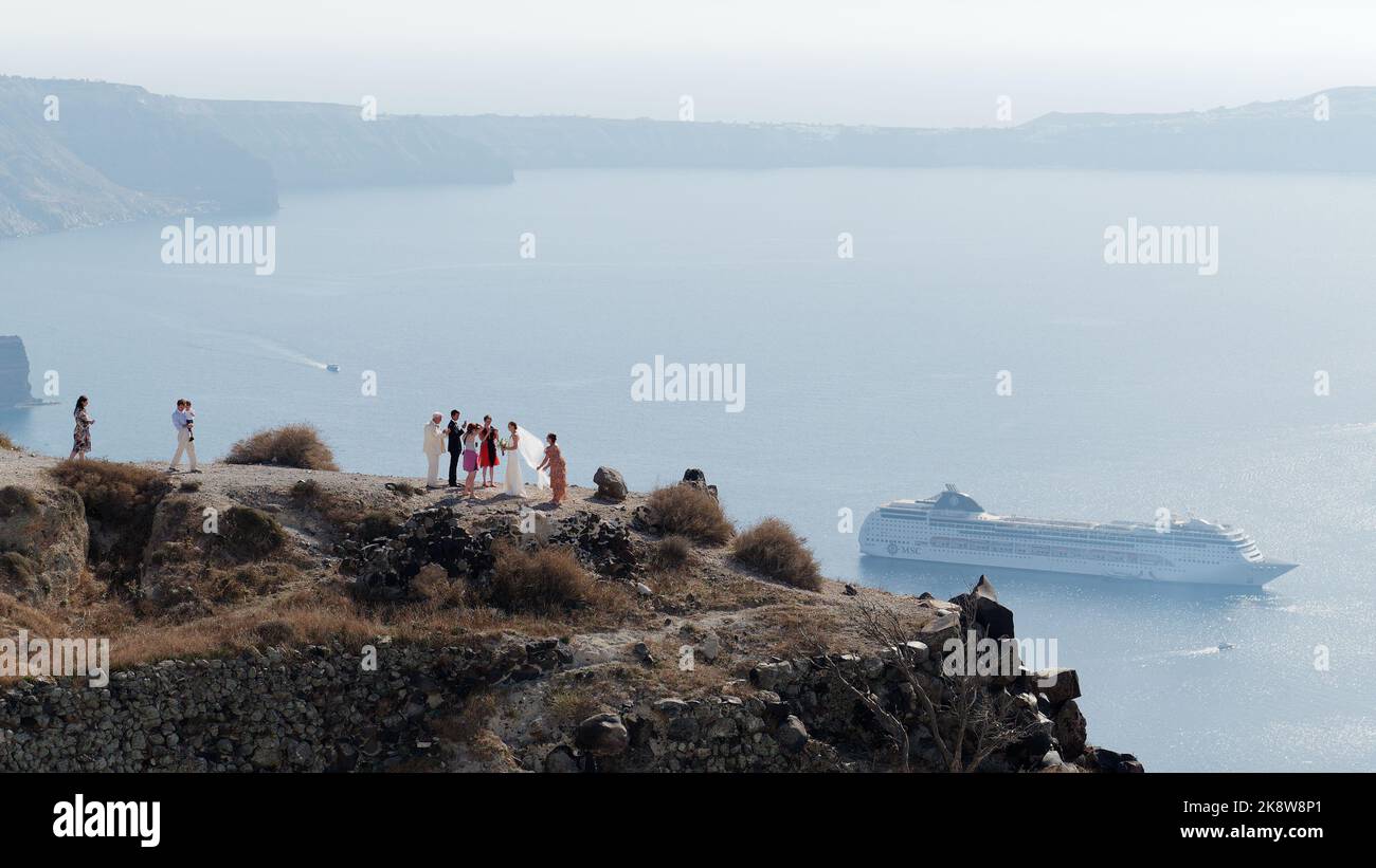 Wedding party on a clifftop overlooking the Caldera with a cruise ship below. Greek Cyclades island of Santorini in the Aegean Sea Stock Photo
