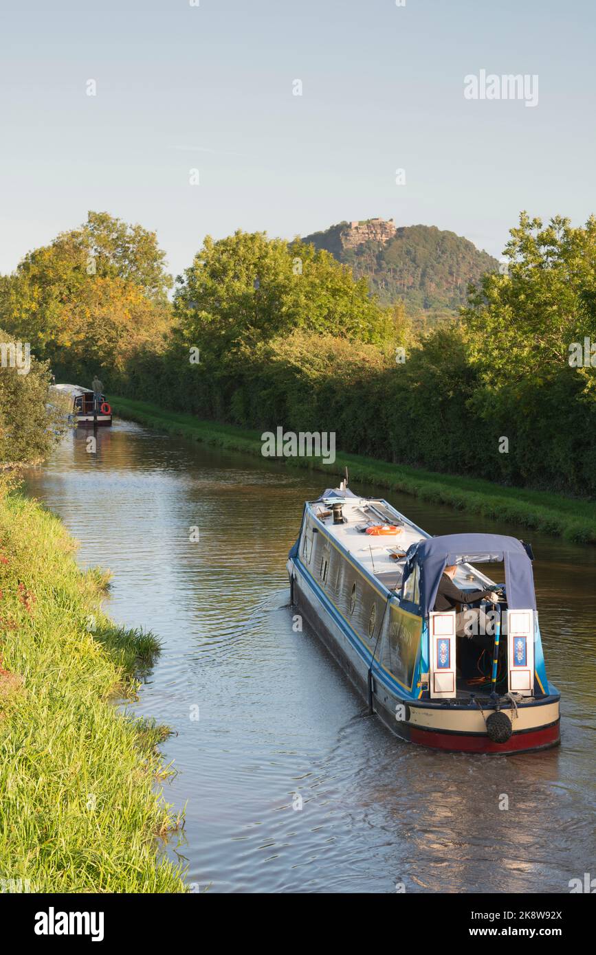 Narrowboats Navigating the Shropshire Union Canal in Cheshire on a Sunny Autumn Evening in Sight of the Rocky Crag of Beeston Castle Stock Photo