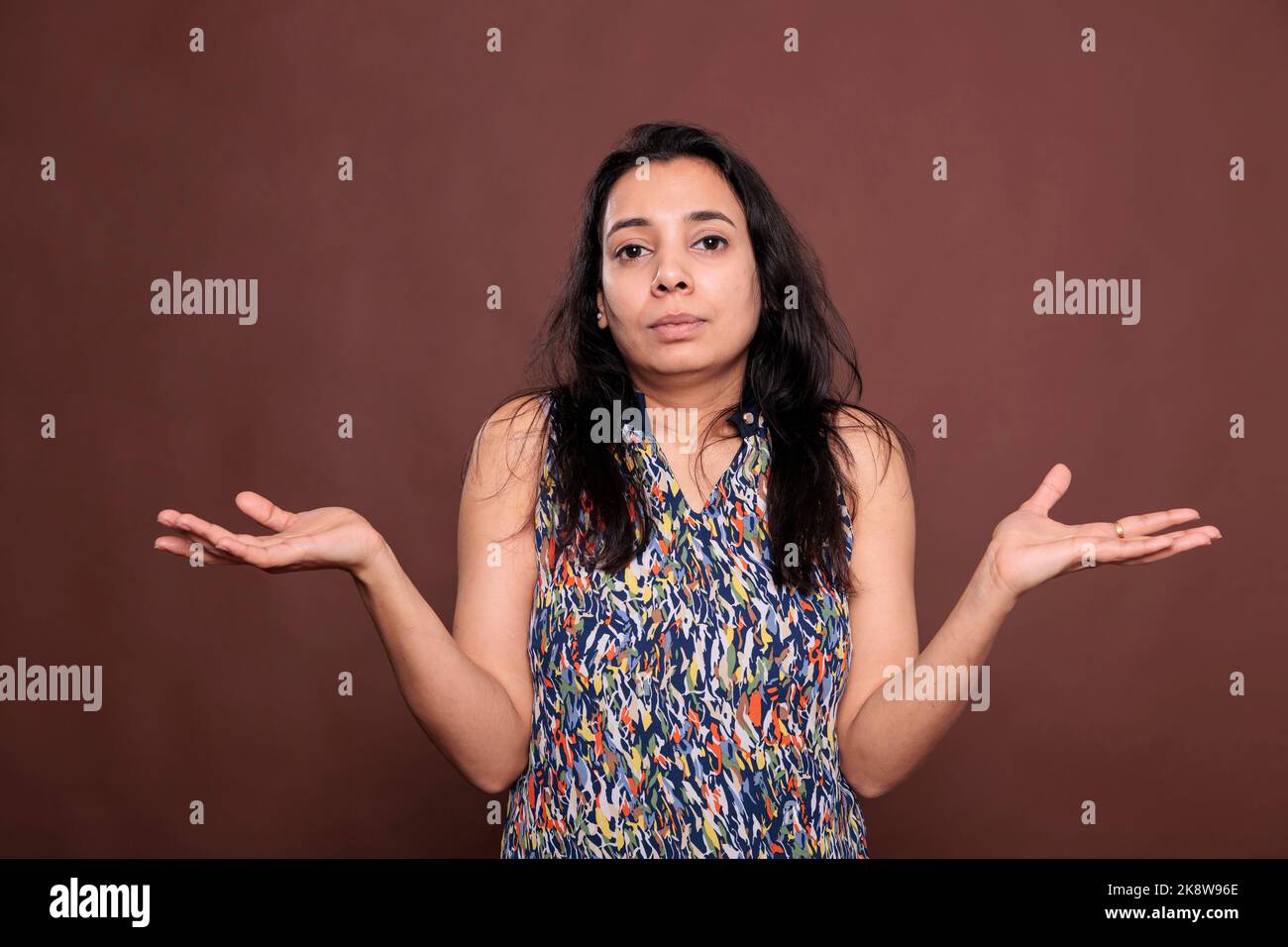 Confused indian woman shrugging shoulders with questioning facial expression portrait. Puzzled lady standing with hands spread wide, doubting, pensive person looking at camera Stock Photo