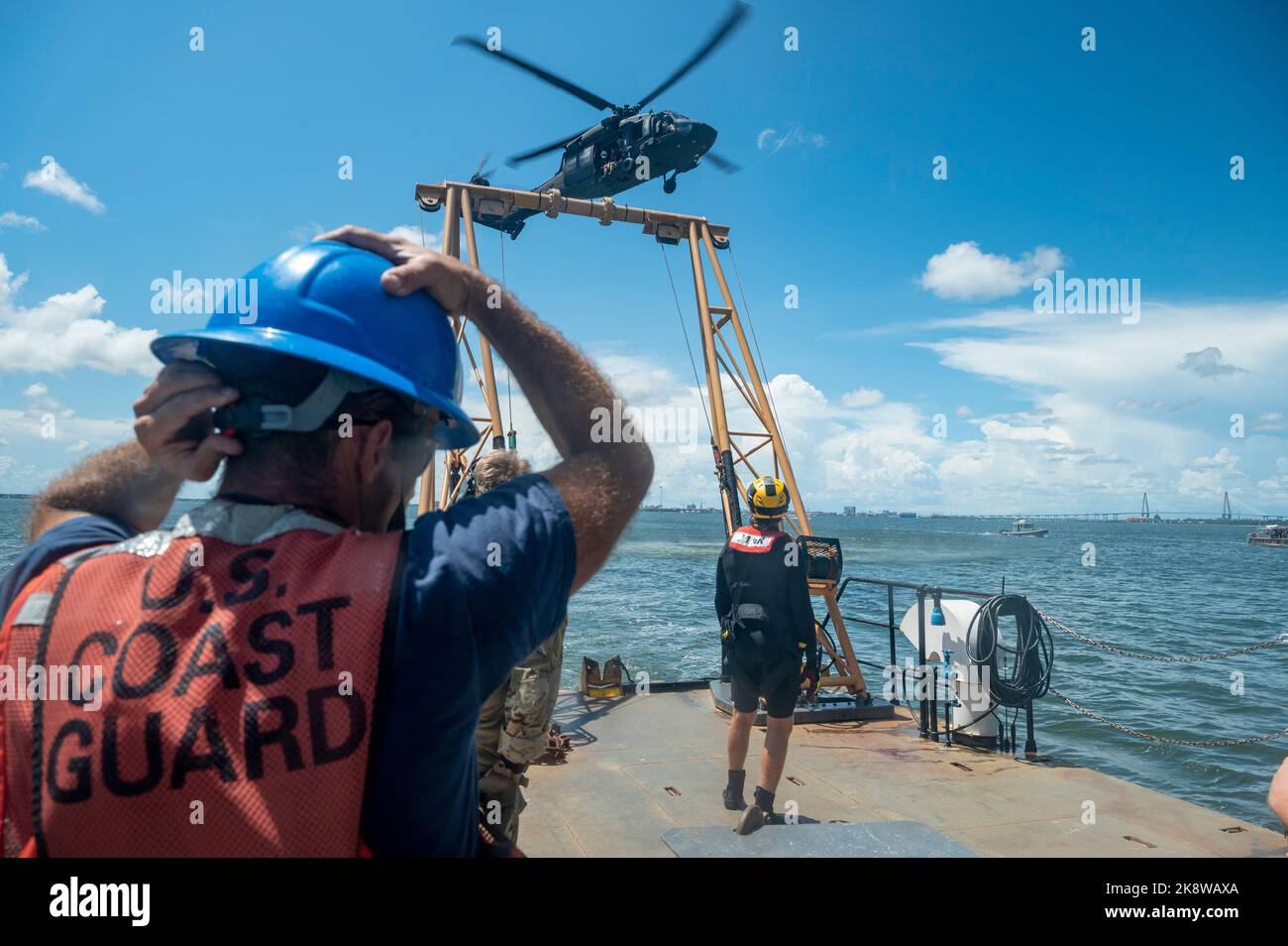 A U.S. Coast Guardsman secures his safety helmet as an H-60M Black Hawk flies overhead during search and rescue training Aug. 4, 2022, in Charleston, South Carolina. Local law enforcement and maritime agencies support training conducted by FBI Hostage Rescue Team (HRT). The Priority 1 Air Rescue team taught rescue procedures for FBI personnel onboard H-60M Black Hawk helicopters. (U.S. Air Force photo by Staff Sgt. Frank Rohrig) Stock Photo