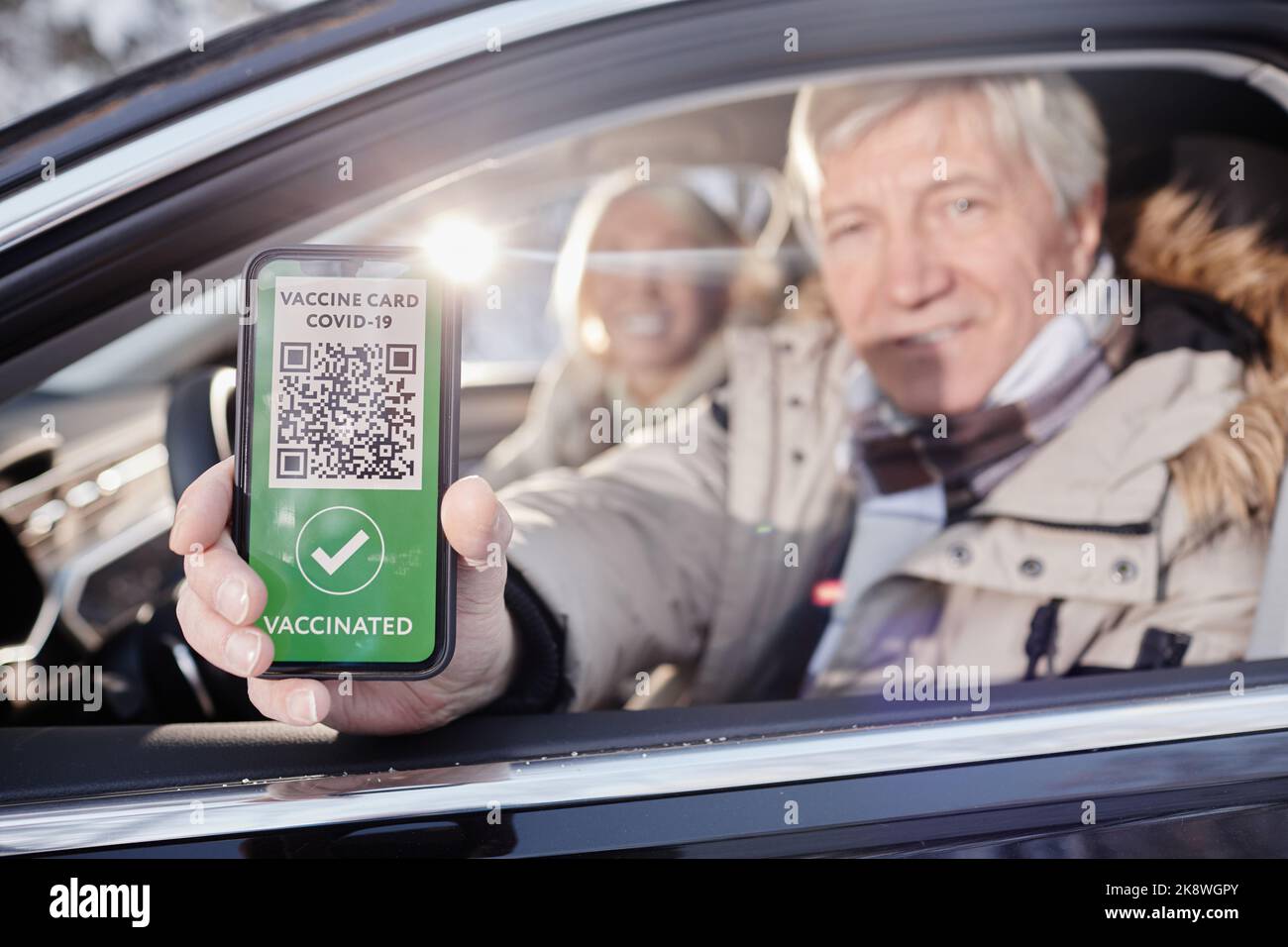 Close up of senior man showing digital vaccination code from car window while enjoying winter vacation, copy space Stock Photo