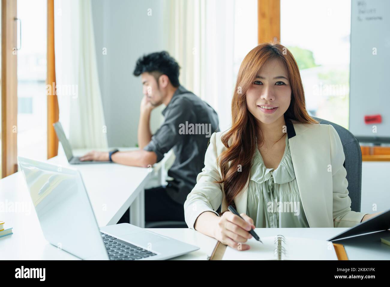 Portrait of an Asian bank employee using notebooks to take notes, budget documents and computers to close financial statements Stock Photo