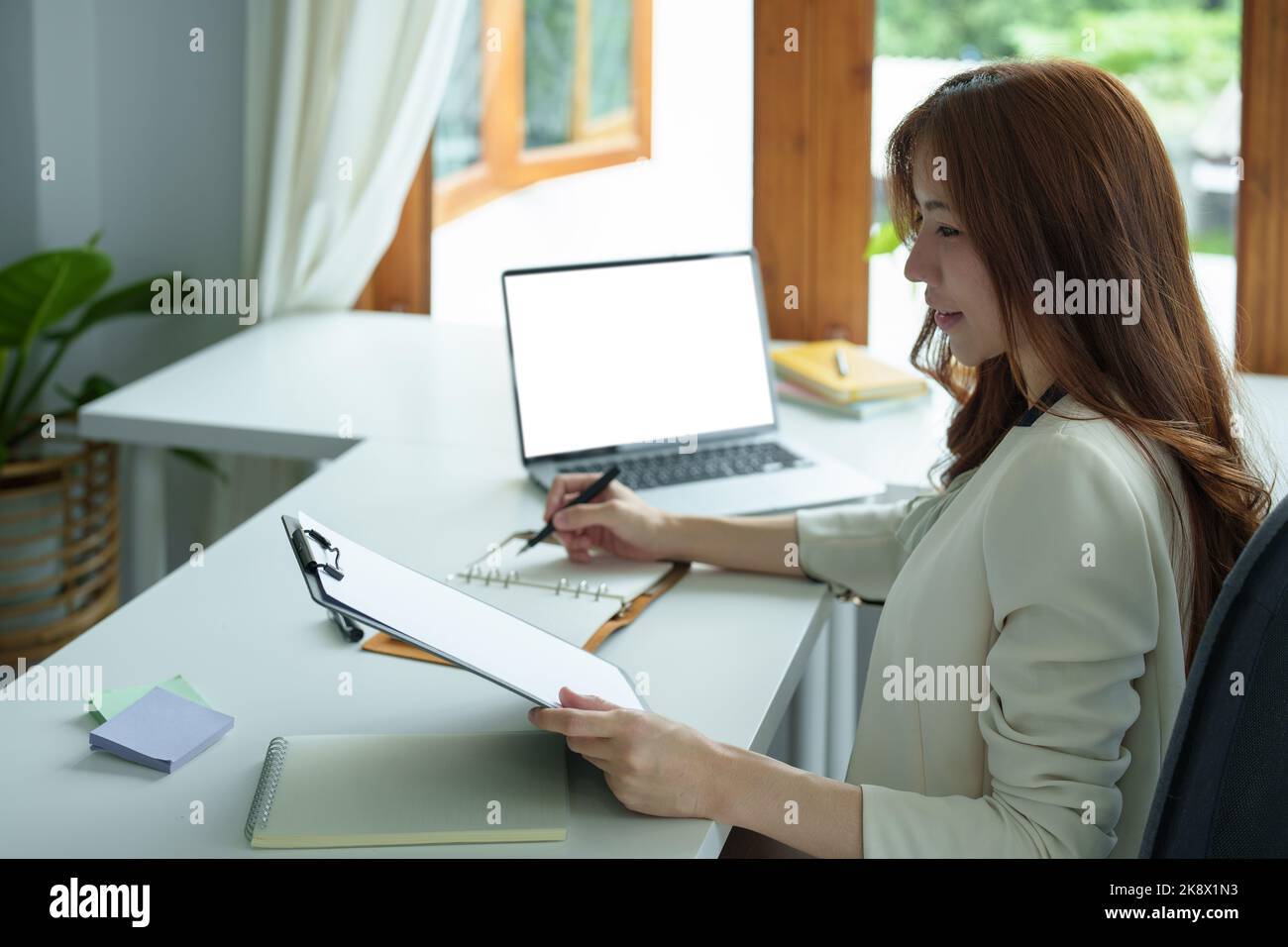 Portrait of an Asian bank employee using notebooks to take notes, budget documents and computers to close financial statements Stock Photo