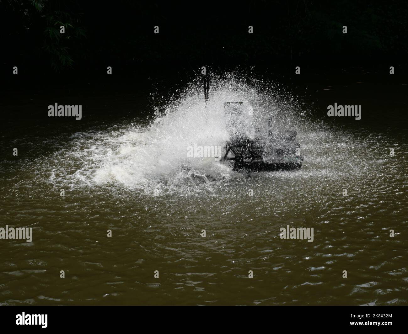 Group of water droplets splashed from the blow of the turbine with black background, Paddle wheel hitting green water surface to add oxygen Stock Photo