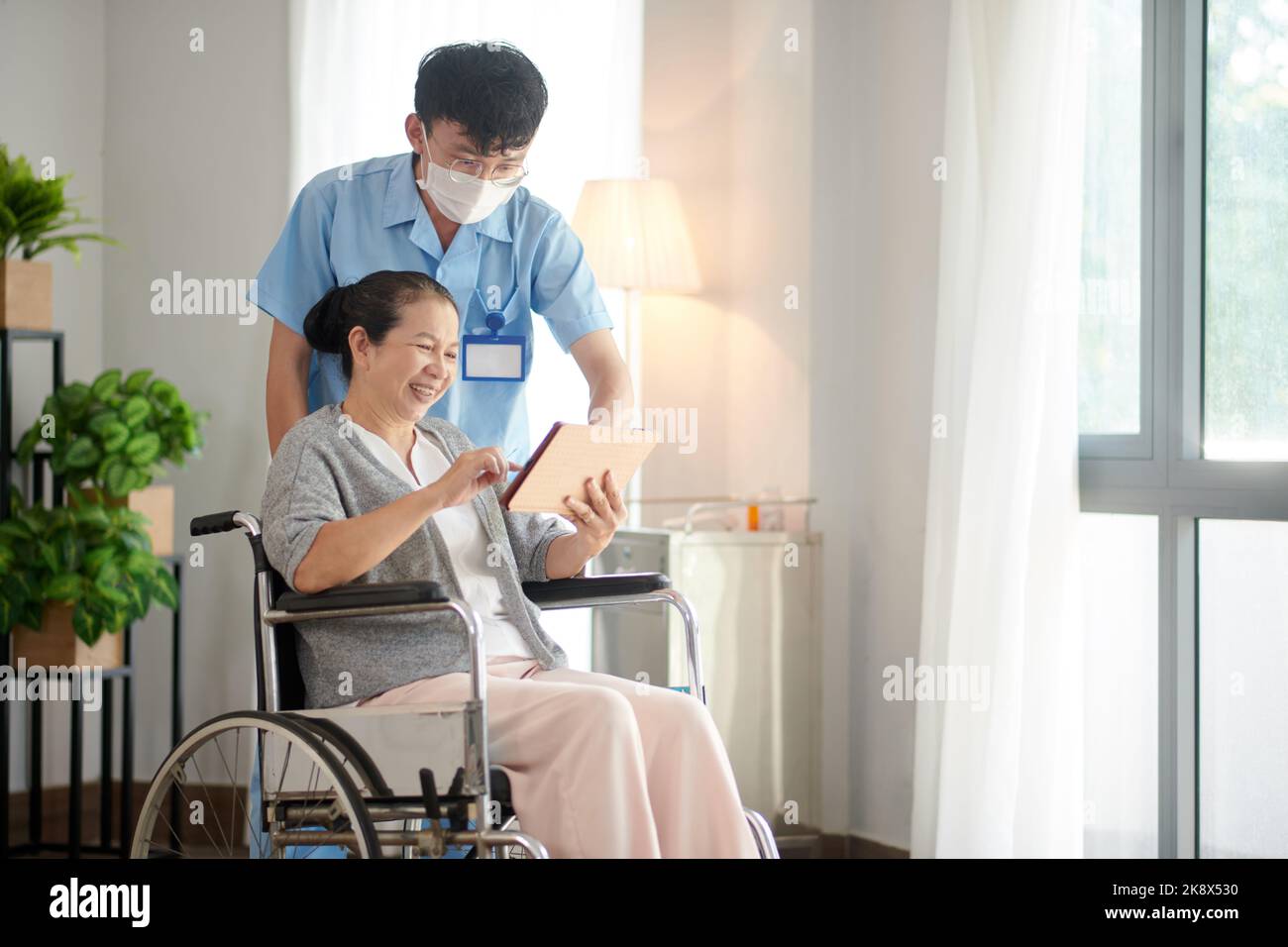 Nursing home worker helping senior patient with application on tablet computer Stock Photo