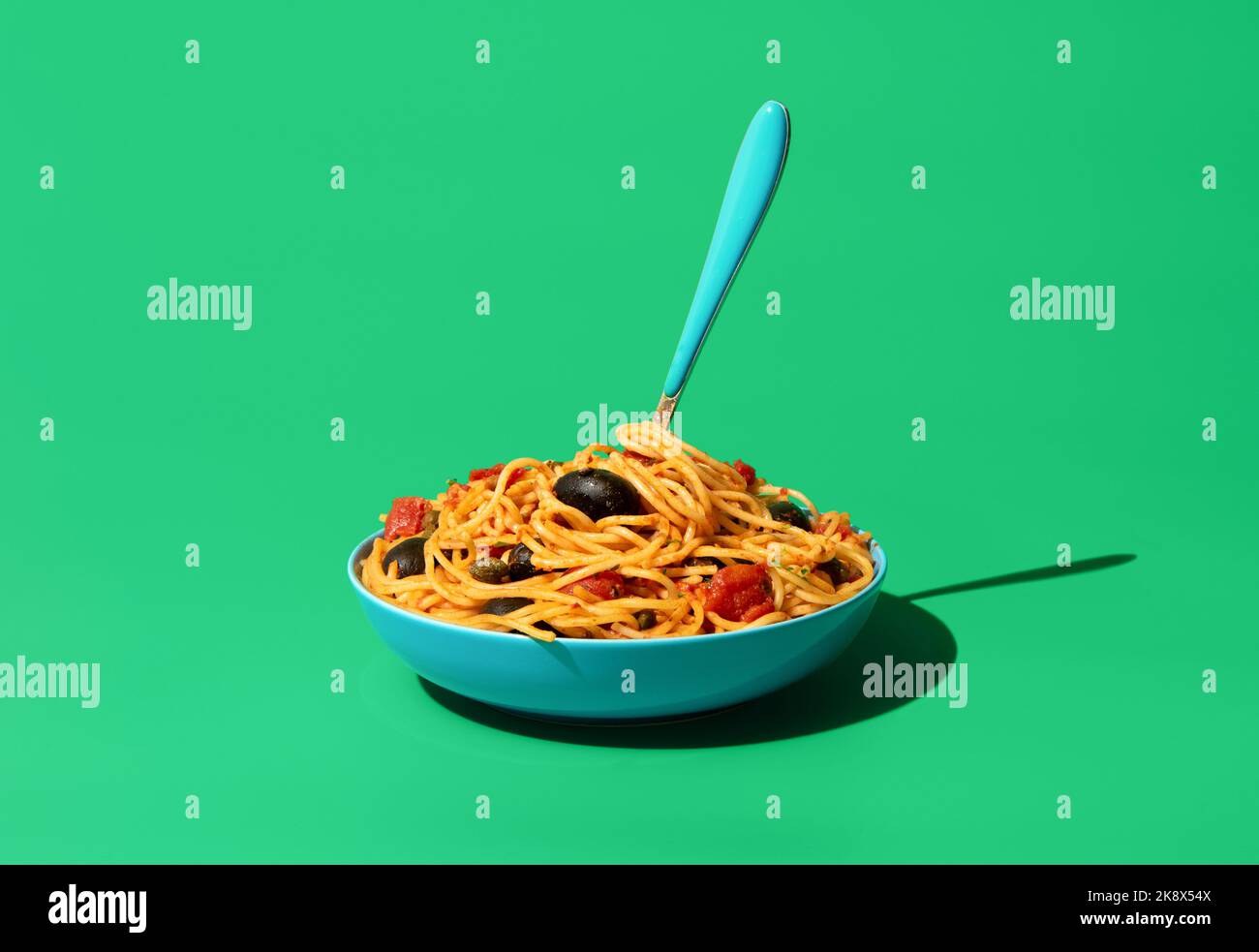 Classic italian pasta, spaghetti puttanesca, minimalist on a green table. Delicious vegetarian pasta dish, spaghetti with tomato sauce, olives, and ca Stock Photo