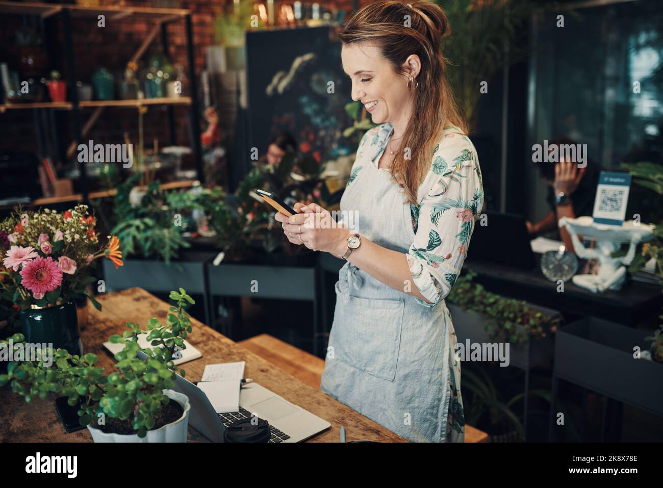 Updating my social media. an attractive young businesswoman standing in her floristry and using her cellphone to photograph her flowers. Stock Photo