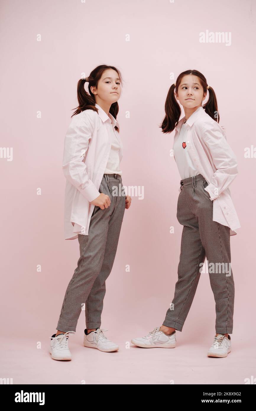 Fashionable twin girls with layered white shirts over pink background. Stock Photo