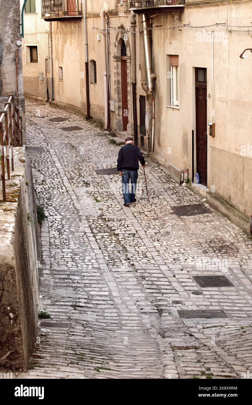 elder man with coppola hat and walking cane on the stone street of medieval village of Prizzi in Western Sicily, Italy Stock Photo