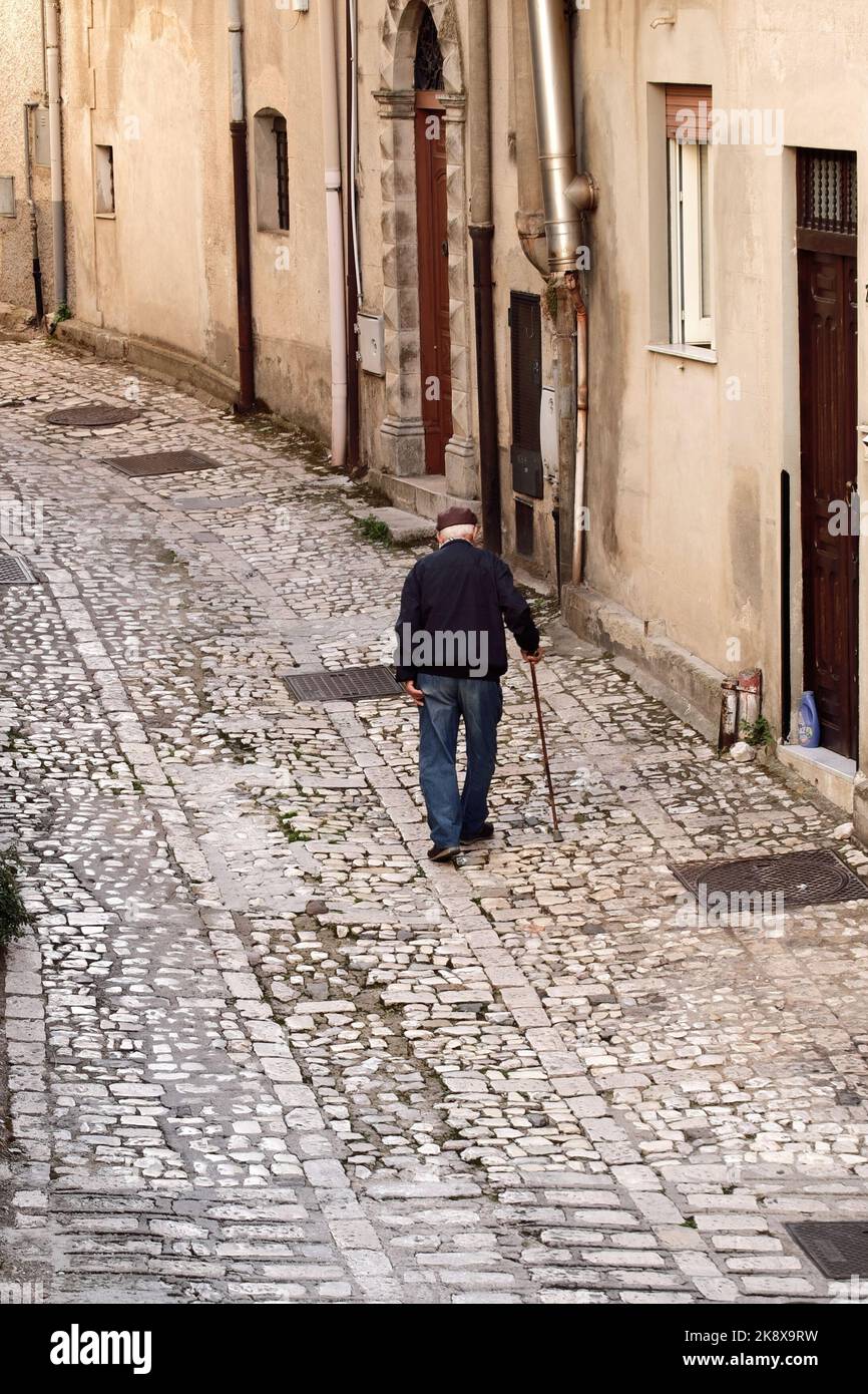 elder man with coppola hat and walking cane on the stone street of medieval village of Prizzi in Western Sicily, Italy Stock Photo