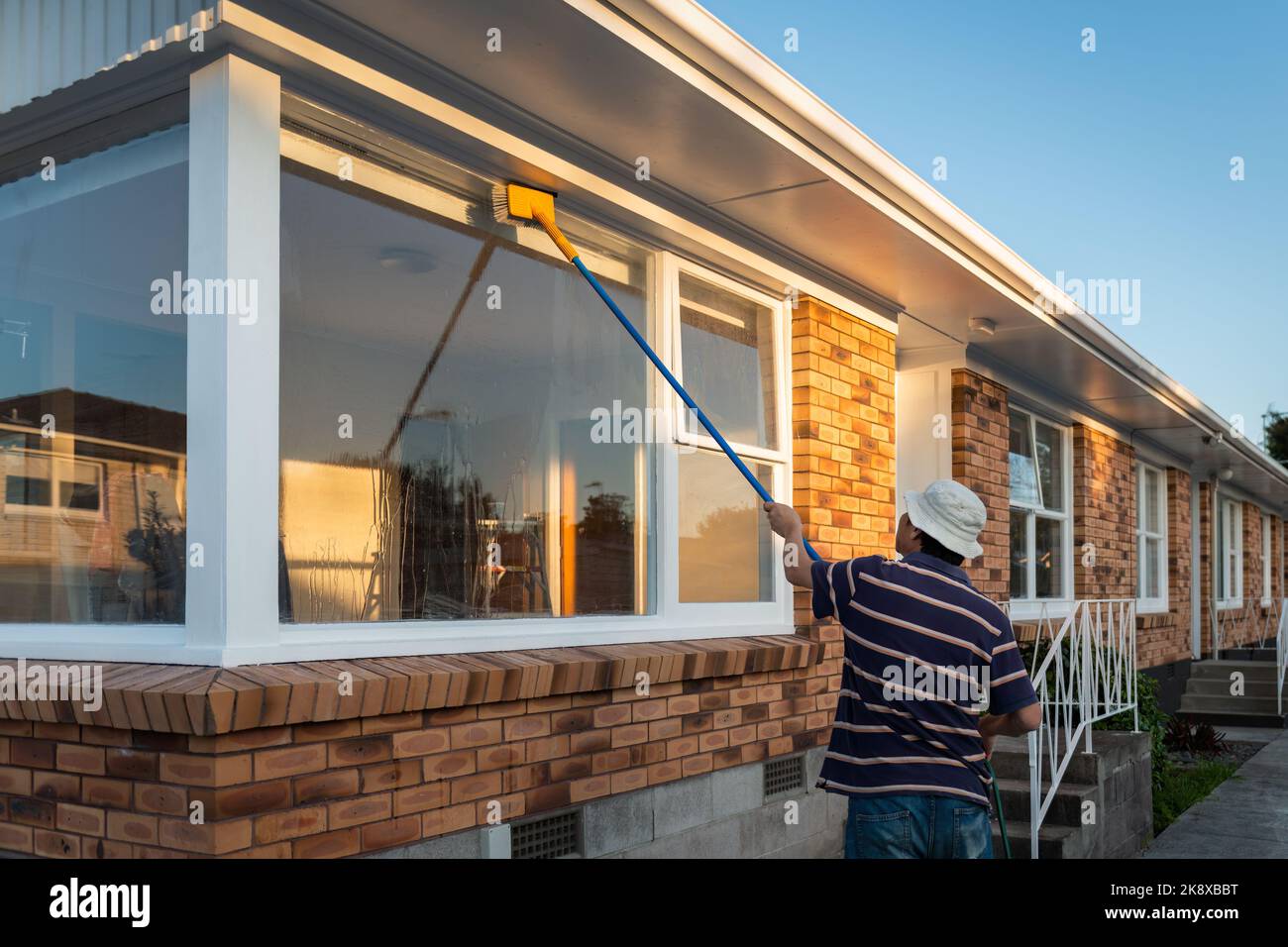 Man washing windows of an empty house with long pole and brush. Home refurbishment project in Auckland. Stock Photo
